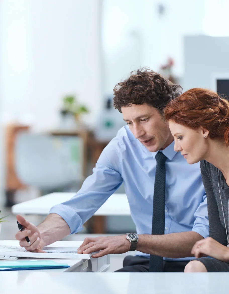 Two ISO 9001 consultants sitting at the desk, checking papers and discussing the latest changes in the project.