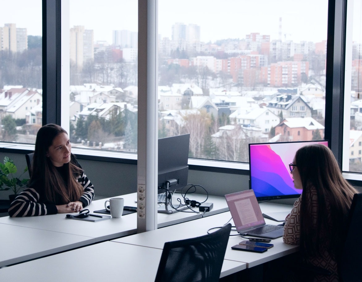 Two persons sitting at their desks and talking to each other.