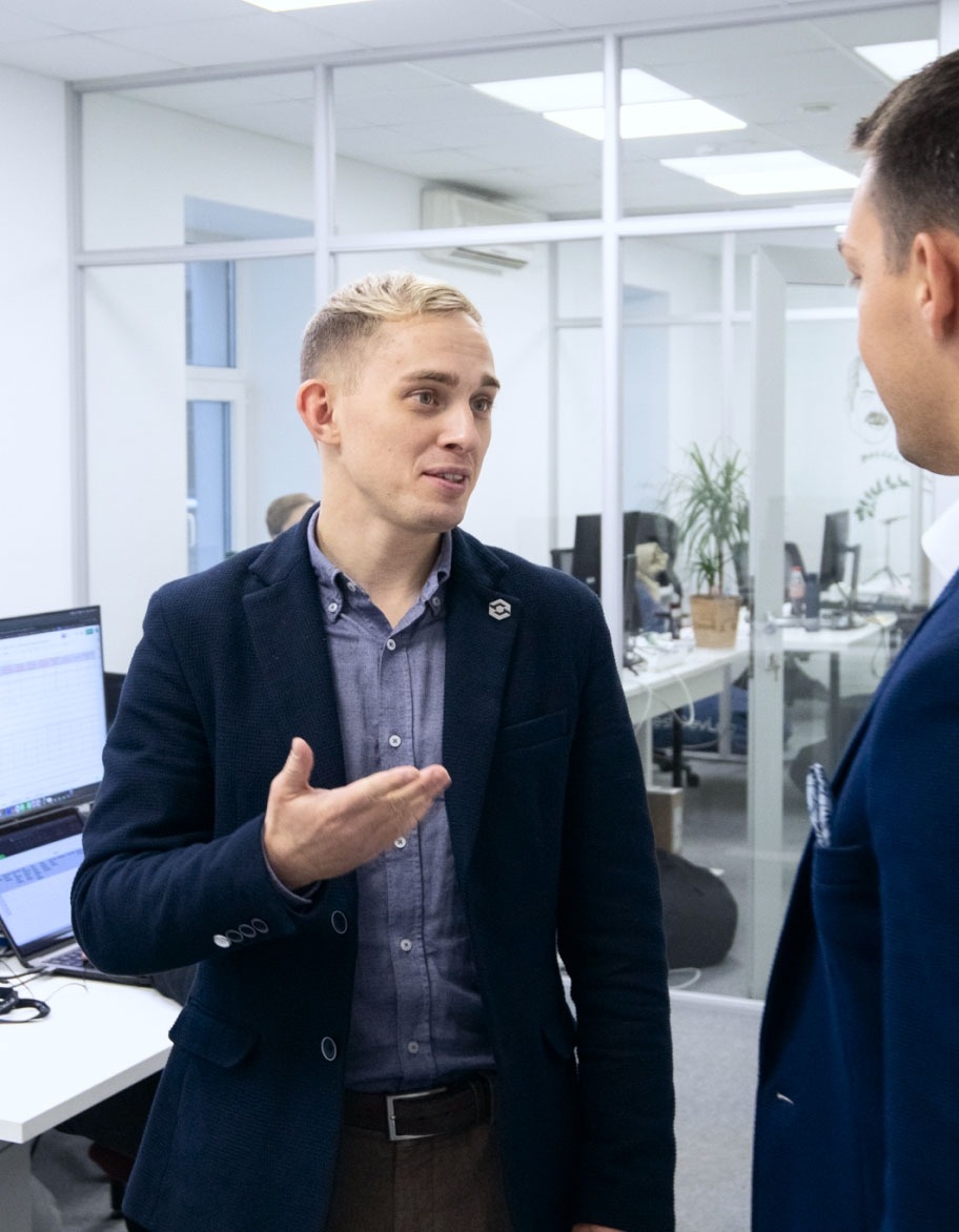 Two persons standing in the office and talking to each other.